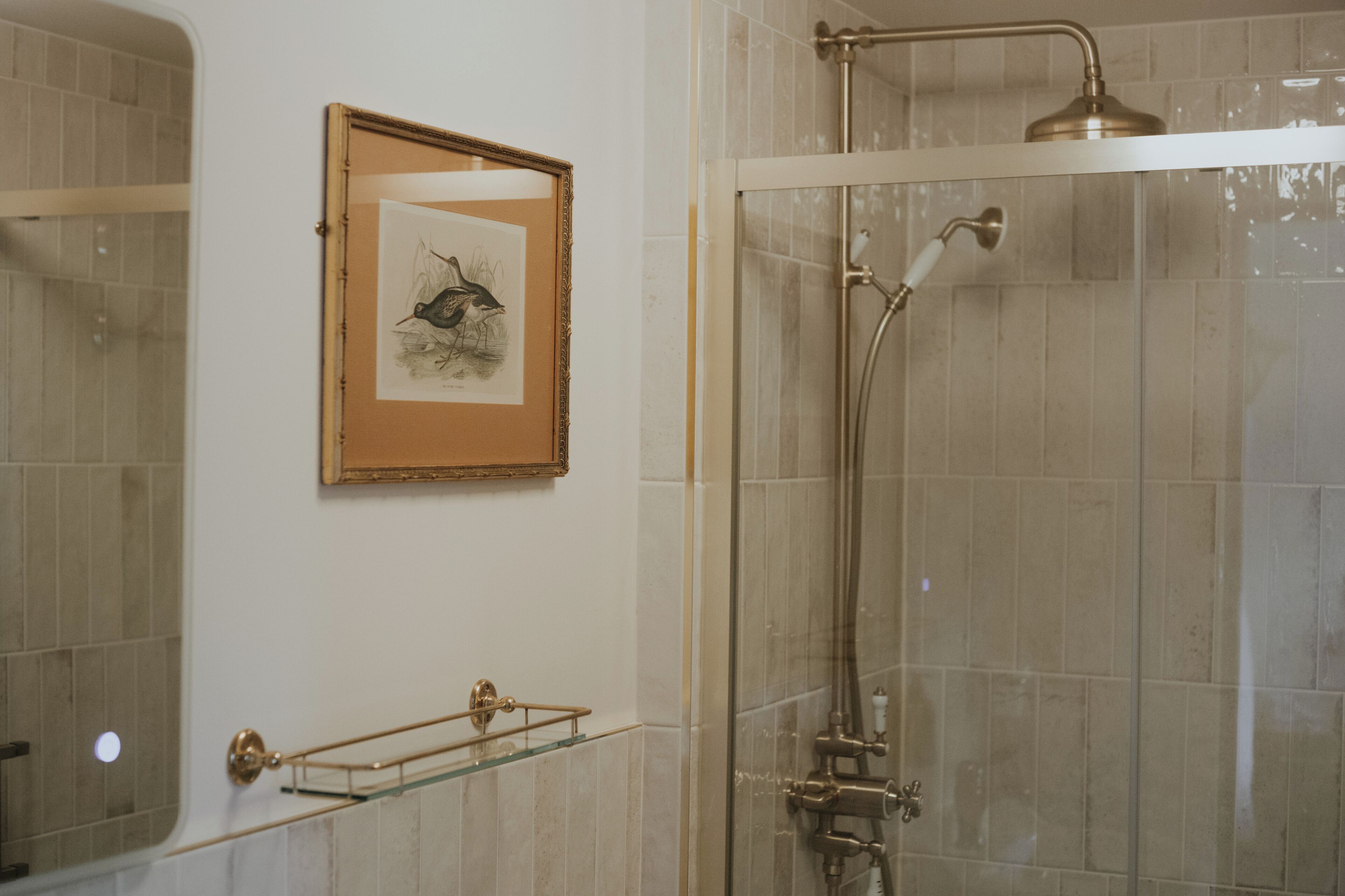 Un baño con cabina de ducha de vidrio, una obra de arte enmarcada en la pared y una repisa de vidrio con toallero.