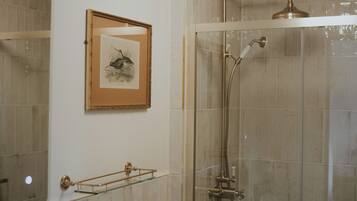 Un baño con cabina de ducha de vidrio, una obra de arte enmarcada en la pared y una repisa de vidrio con toallero.