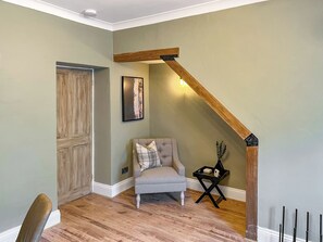 A room with a wooden door, a gray armchair, a small table with a vase, and a wooden beam ceiling. - 2 bedroom accommodation in Barnard Castle (Barnard Castle)