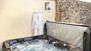 Un bain à remous avec un mur en pierre en arrière-plan, un porte-serviettes et un luminaire fixé au mur.