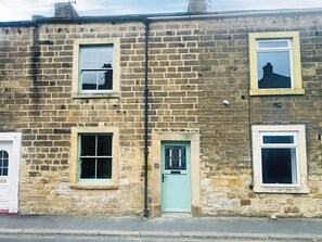 A two-story stone building with a green door, two windows with white frames, and a small balcony with a railing. - 2 bedroom accommodation in Barnard Castle (Barnard Castle)