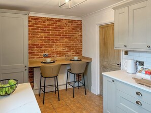 A compact kitchen with a brick wall, two bar stools, a white countertop, and a coffee maker. - 2 bedroom accommodation in Barnard Castle (Barnard Castle)