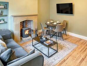 A living room with a fireplace, a sofa, a coffee table, and a dining area with chairs and a table set for a meal. - 2 bedroom accommodation in Barnard Castle (Barnard Castle)