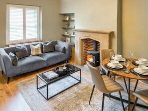 A living room with a gray sofa, a coffee table, a fireplace, and a dining area with a table set for four. - 2 bedroom accommodation in Barnard Castle (Barnard Castle)