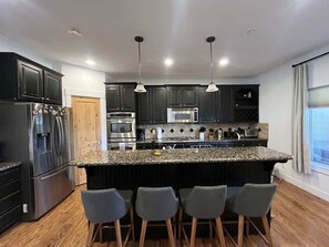Une cuisine moderne avec des meubles de couleur sombre, des appareils électroménagers en acier inoxydable, un plan de travail en granit et des tabourets de bar.
