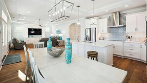 Une cuisine moderne avec des meubles blancs, un îlot central et un coin repas comprenant une table et des chaises blanches.