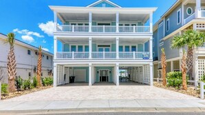 Un hôtel en bord de mer, composé de plusieurs étages, doté d’une entrée couverte, de balcons et d’une enseigne indiquant qu’il propose des locations de vacances.
