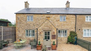 A stone house with a central door, two windows on either side, and a small garden area with a table and chairs. - Stunning property in the beautiful market town of Stow-on-the-Wold - Devon House Cottage (Stow-on-the-Wold)