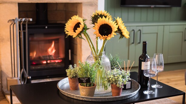 A table with a vase of sunflowers, potted plants, a bottle of wine, and two wine glasses. - Stunning property in the beautiful market town of Stow-on-the-Wold - Devon House Cottage (Stow-on-the-Wold)