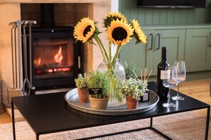 A table with a vase of sunflowers, potted plants, a bottle of wine, and two wine glasses.