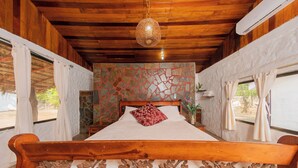 A wooden-framed bed with a decorative headboard, a stone-patterned wall, and a hanging light fixture. - Somar Surf lodge (León)