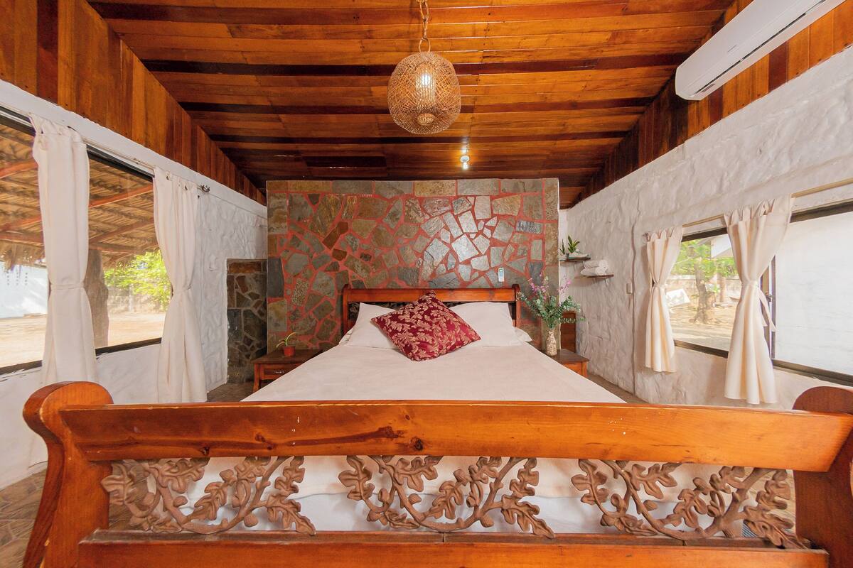 Un lit à cadre en bois avec une tête de lit décorative, un mur imitant la pierre et un luminaire suspendu.