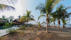 A beach area with palm trees, a small structure, and a pool. - Somar Surf lodge (León)