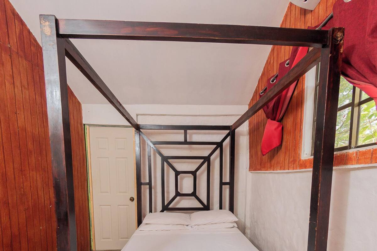 Une chambre individuelle avec un lit superposé en bois, une fenêtre avec des rideaux rouges et une porte blanche.
