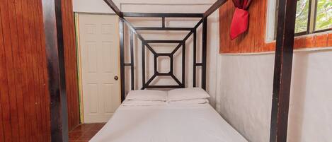 A single-occupancy room with a wooden bunk bed, a window with red curtains, and a white door.