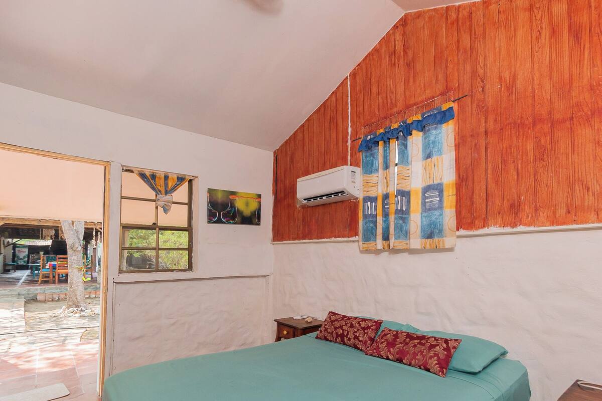 Une chambre à coucher avec un lit, une fenêtre avec des rideaux, un ventilateur de plafond et un mur en bois.