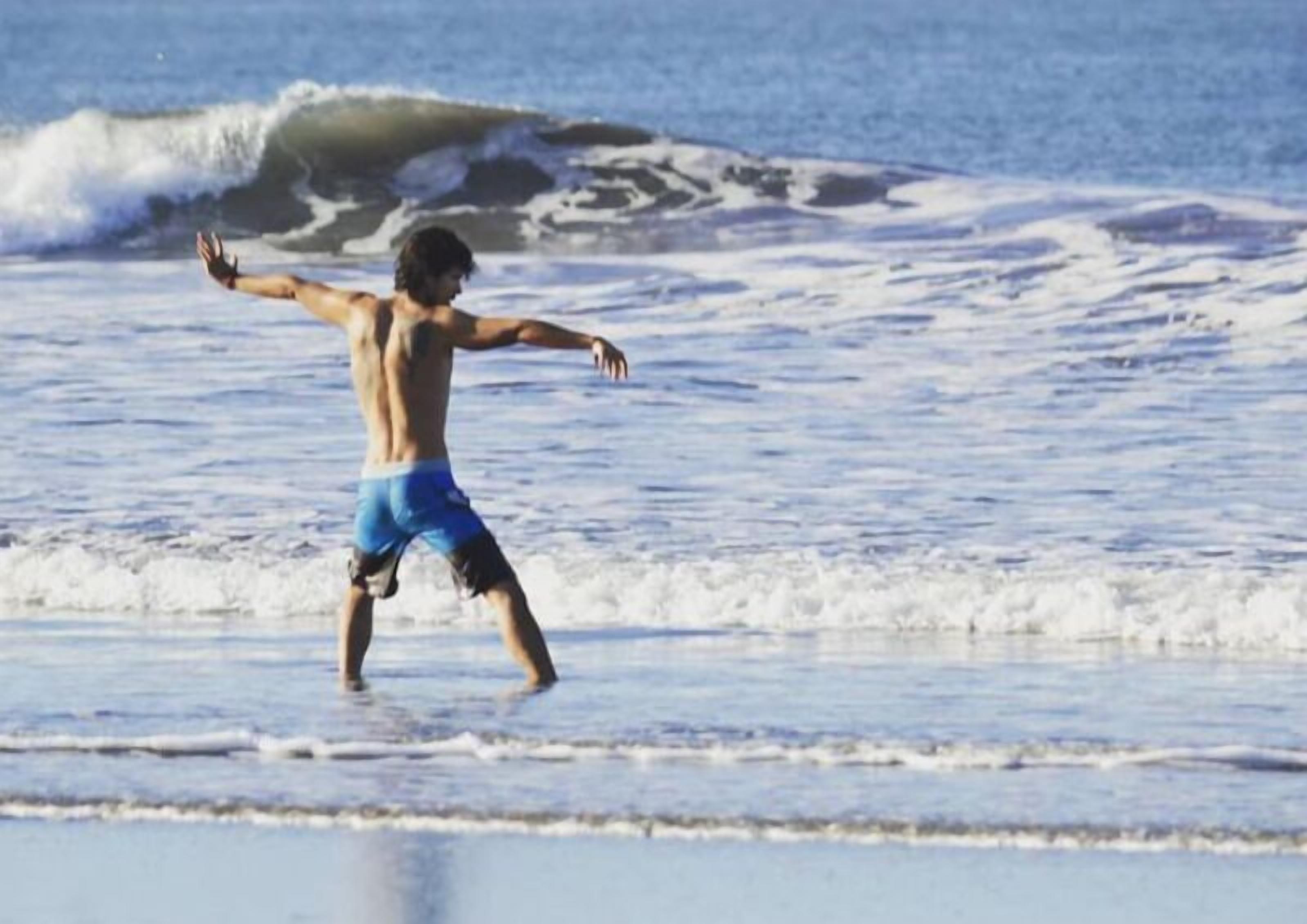 A person in blue swim trunks on a beach with waves.