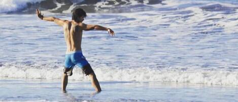 A person in blue swim trunks on a beach with waves.