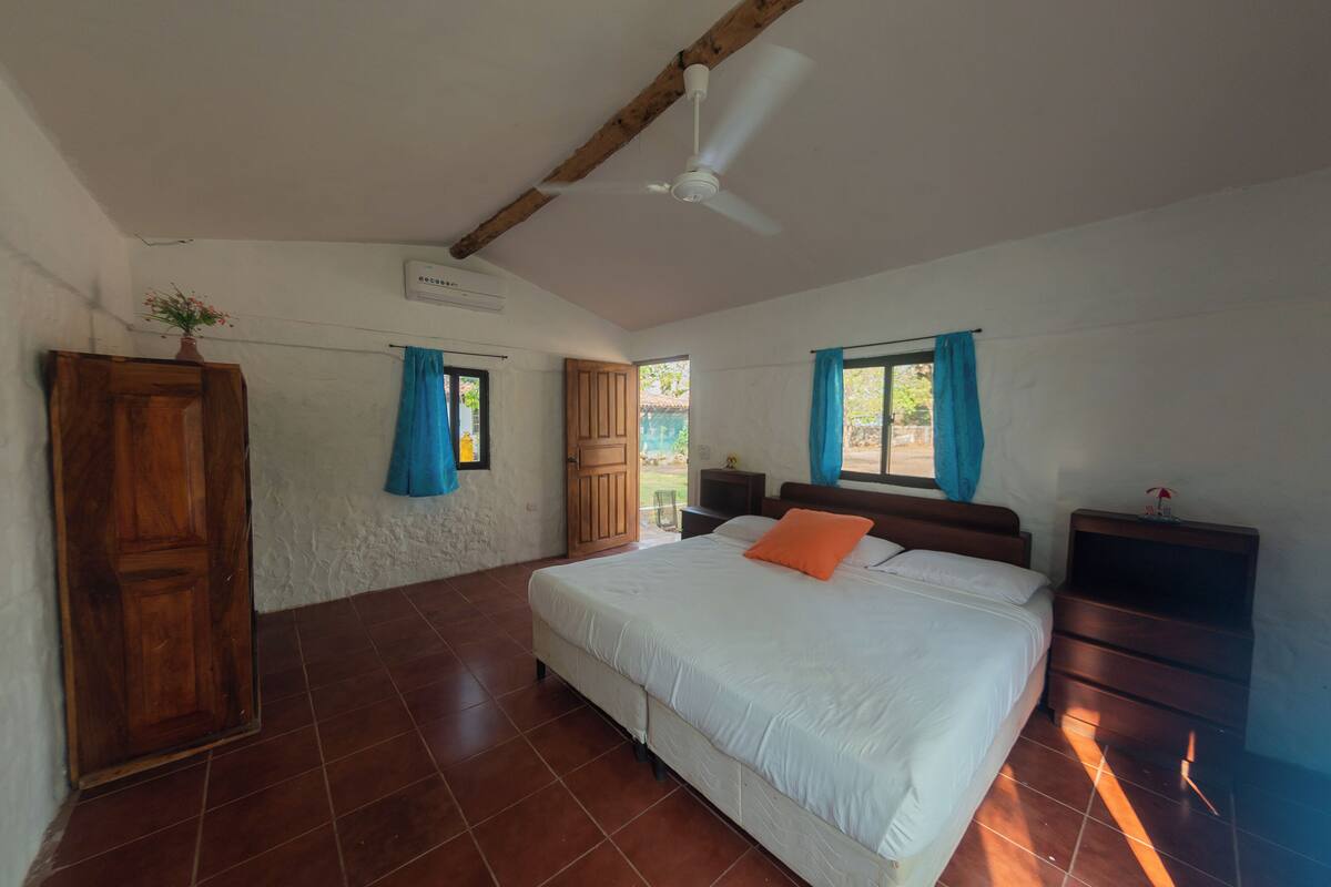 Une chambre à coucher avec un lit, une armoire en bois, un ventilateur de plafond et une fenêtre avec des rideaux.