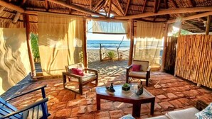 A beachside room with a thatched roof, two chairs, a table, and a view of the ocean. - Somar Surf lodge (León)