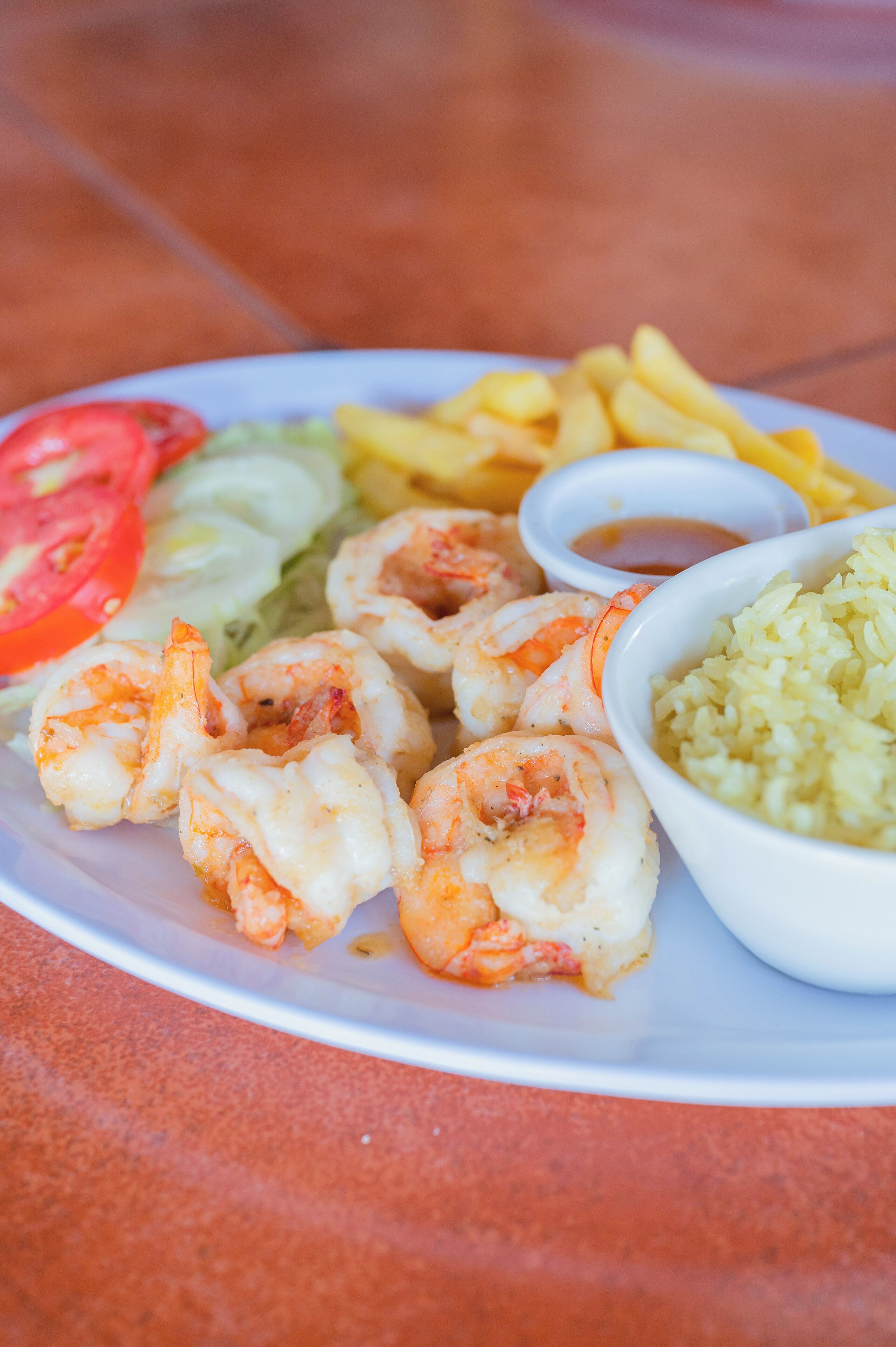 A plate with shrimp, fries, rice, and a small bowl of sauce.