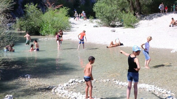 Un entorno natural con un acantilado rocoso, agua cristalina y personas practicando deportes acuáticos.