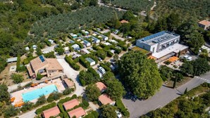 Vista aérea de un camping con vehículos recreativos, una piscina y un edificio grande con paneles solares.