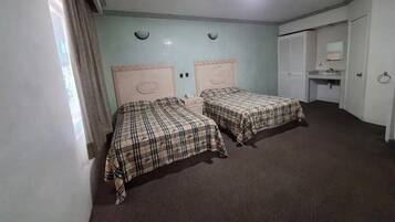 Una habitación con dos camas, una lámpara en el techo, una mesita de noche pequeña y una puerta que da al baño.