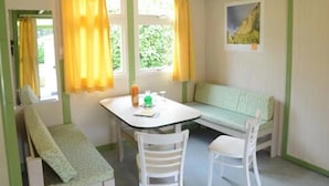 Una habitación pequeña y acogedora, con una decoración verde y blanca, que incluye una mesa, dos sillas, un banco y una ventana con cortinas amarillas.