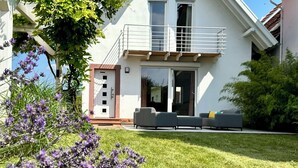 A modern two-story house with a balcony, a sliding glass door entrance, and a small garden area with lavender plants. - Wine and forest, cozy vacation home with outdoor sauna and a big garden (Landau in der Pfalz)