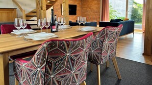 A dining area with a wooden table set for six, patterned chairs, a wine bottle, and a clock on the wall. - Wine and forest, cozy vacation home with outdoor sauna and a big garden (Landau in der Pfalz)