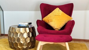 A red velvet armchair with a wooden base and a yellow pillow, positioned next to a hexagonal metallic side table with books on it. - Wine and forest, cozy vacation home with outdoor sauna and a big garden (Landau in der Pfalz)