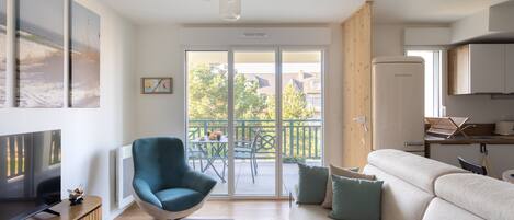 A modern living room with a sofa, a teal armchair, a flat-screen TV, and a sliding glass door leading to an outdoor patio.