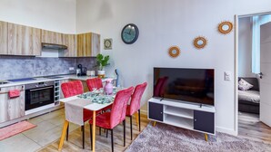 Una cocina moderna con armarios de madera, un comedor con sillas rojas, un televisor y decoración en las paredes.