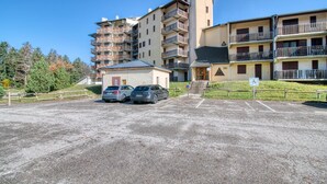 A multi-story parking lot with several cars parked, a building with balconies, and a small entrance building. - Le Cocon des 3 Domaines - Appt pour 4 (Ax-les-Thermes)