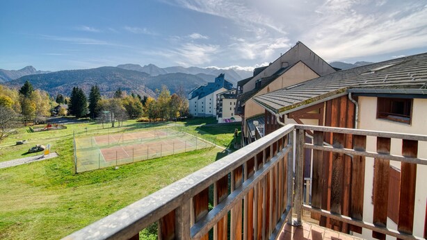 A residential area with a tennis court, mountains in the background, and a building with a balcony. - Le Cocon des 3 Domaines - Appt pour 4 (Ax-les-Thermes)