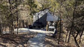 A concrete pathway leading to a stone building with a metal roof, surrounded by trees.