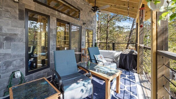 A covered outdoor seating area with stone walls, large windows, and a ceiling fan.