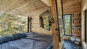 A wooden cabin interior with a bed, a window, and a shelf with items.