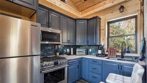 A modern kitchen with stainless steel appliances, blue cabinets, and a window overlooking the outdoors.