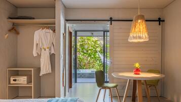 Un dormitorio moderno con cama, mesita de noche y un pequeño armario. Se ve una ventana con vistas a la vegetación.