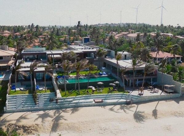 A resort with a swimming pool, palm trees, and wind turbines in the background. - Saline Taíba Boutique Beach Hotel (São Gonçalo do Amarante)