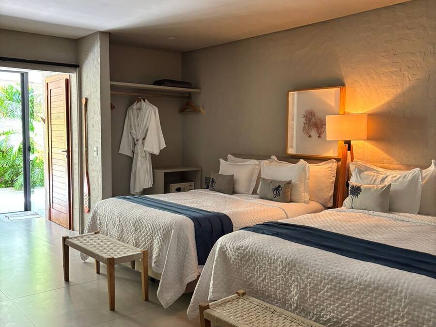 Habitación de hotel con dos camas, un banco, una bata y una lámpara.