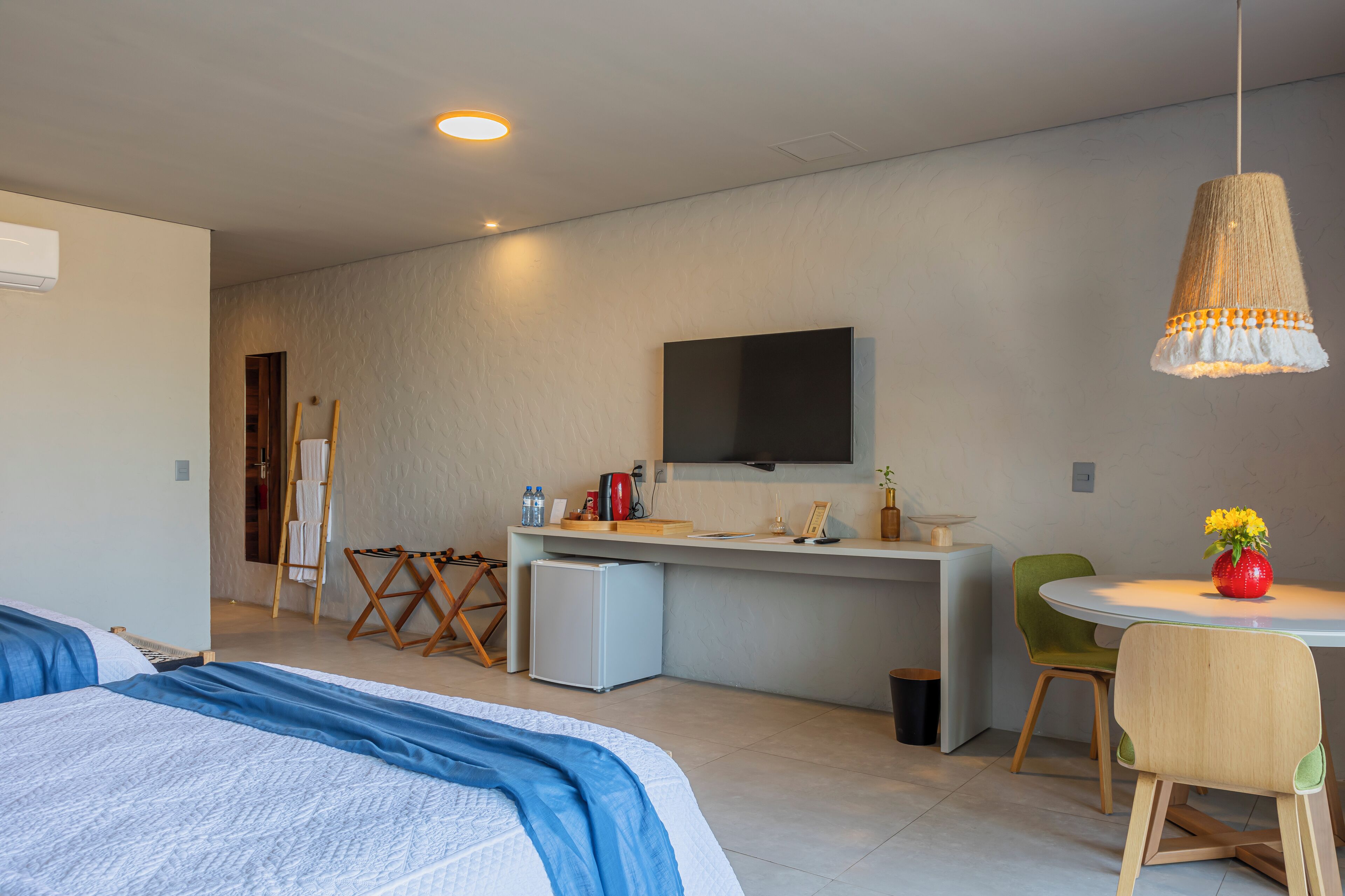 Quarto de hotel moderno com uma cama, uma pequena escrivaninha com televisão, uma cadeira e uma mesa com um vaso de flores.