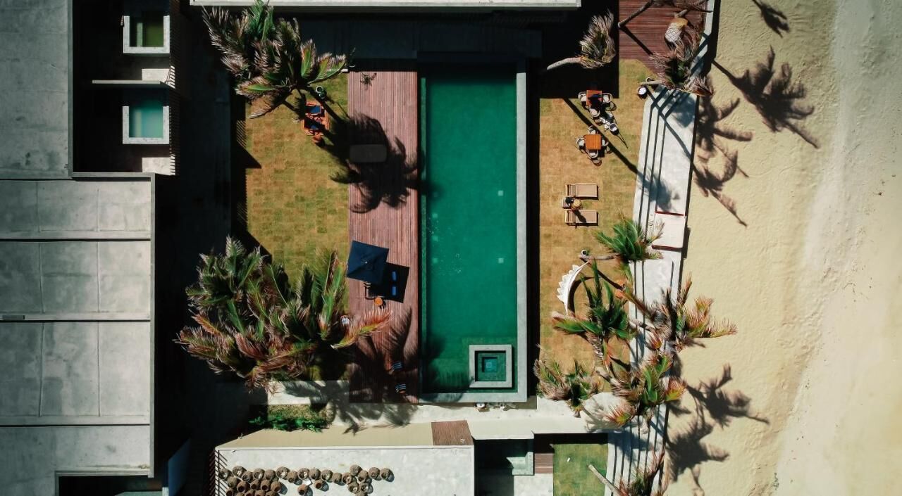 An aerial view of a modern hotel with a swimming pool, outdoor seating, and palm trees.