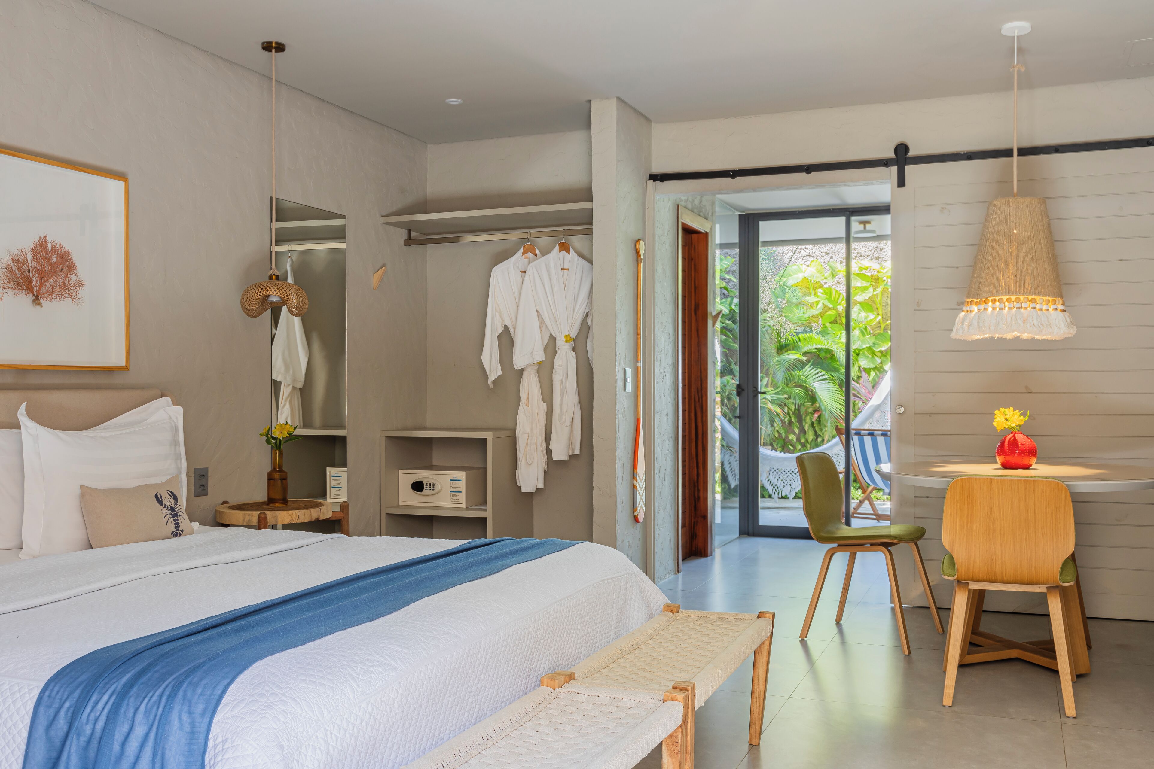 Habitación de hotel moderna con una cama grande, una zona de estar con sillas, una mesita con un jarrón y vistas al exterior.
