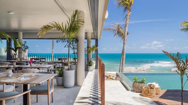 Een terras met tafels en stoelen, palmbomen en uitzicht op de oceaan.