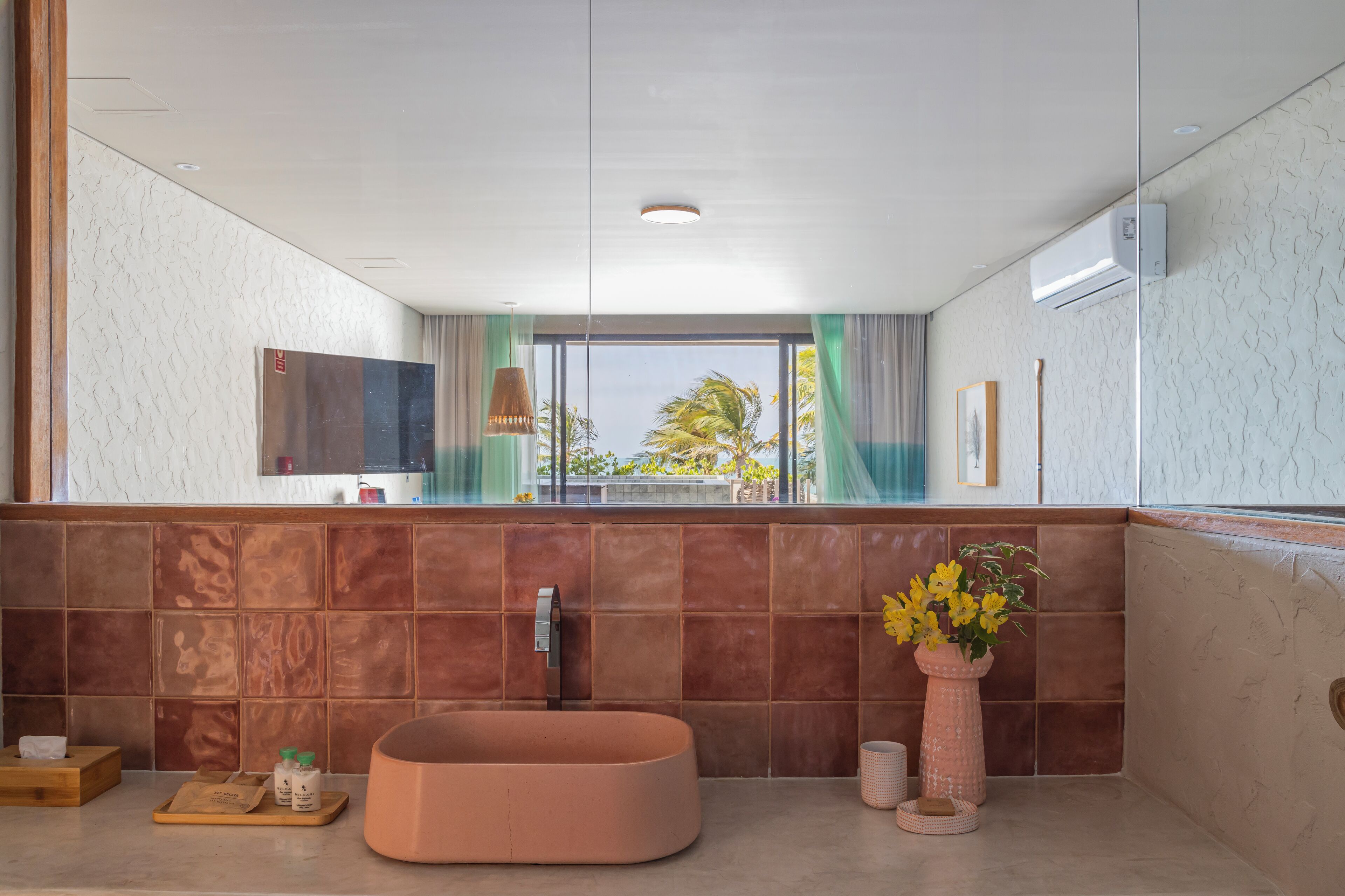 A modern bathroom with a large window, a bathtub, a vanity with a mirror, and a vase with flowers.