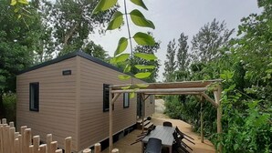 Una terraza de madera con una mesa, sillas, una cabaña pequeña y una estructura de pérgola.