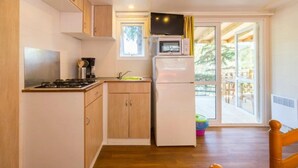 Eine kleine Küche mit Holzausstattung, einer Mikrowelle, einem Kühlschrank und einem Fenster mit Blick auf einen Balkon.